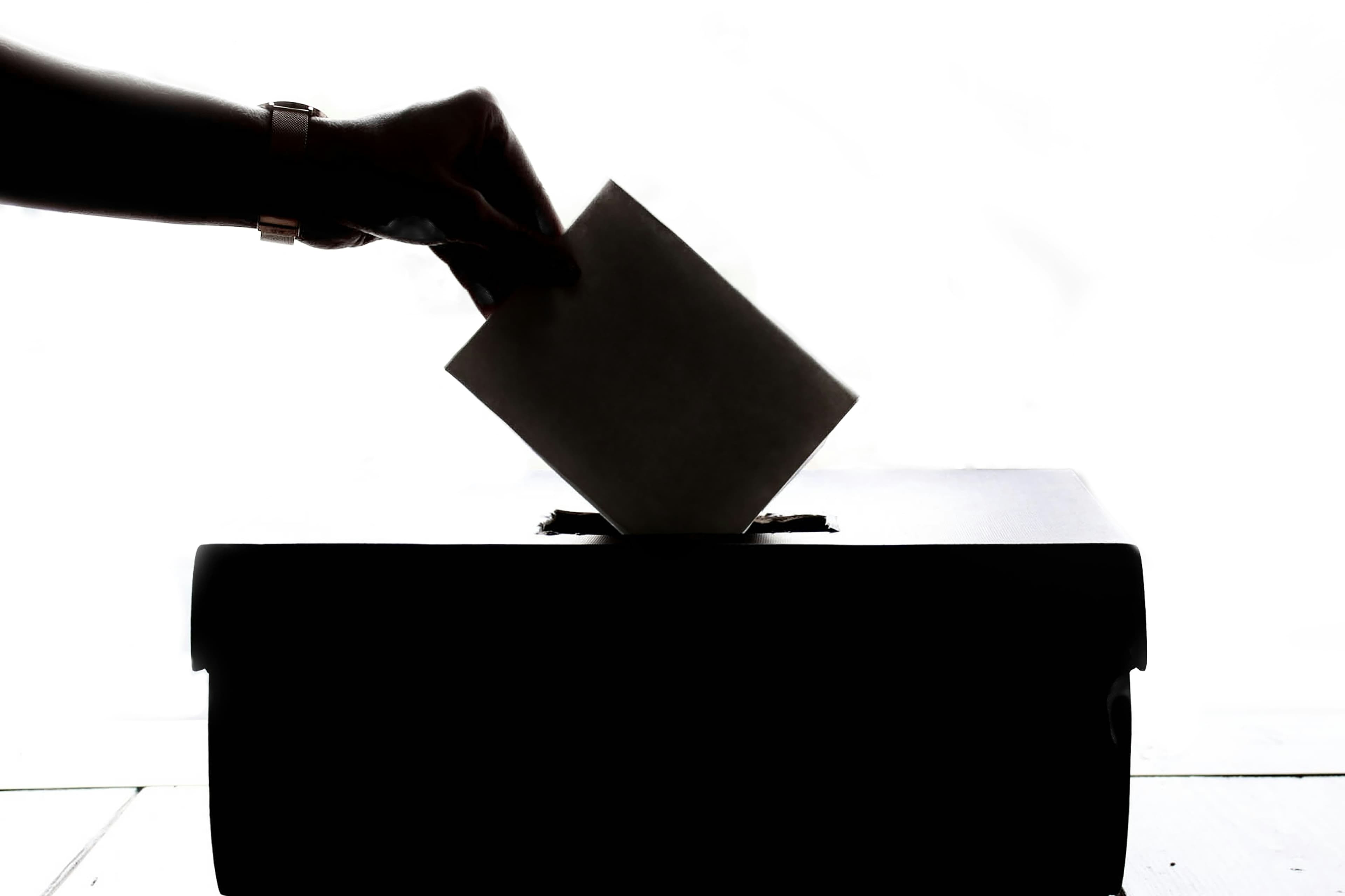 A hand in silhouette dropping a ballot into a ballot box